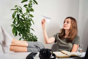 Ragazza in ufficio con le gambe sulla scrivania che lancia un aeroplano di carta: distrazione