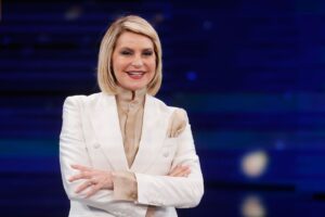 Simona Ventura che sorride con braccia incrociate e completo bianco