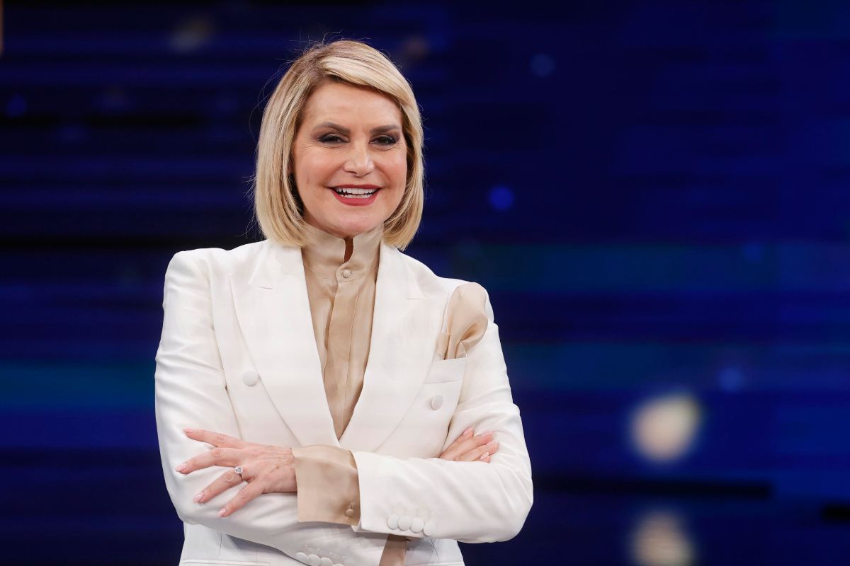 Simona Ventura che sorride con braccia incrociate e completo bianco