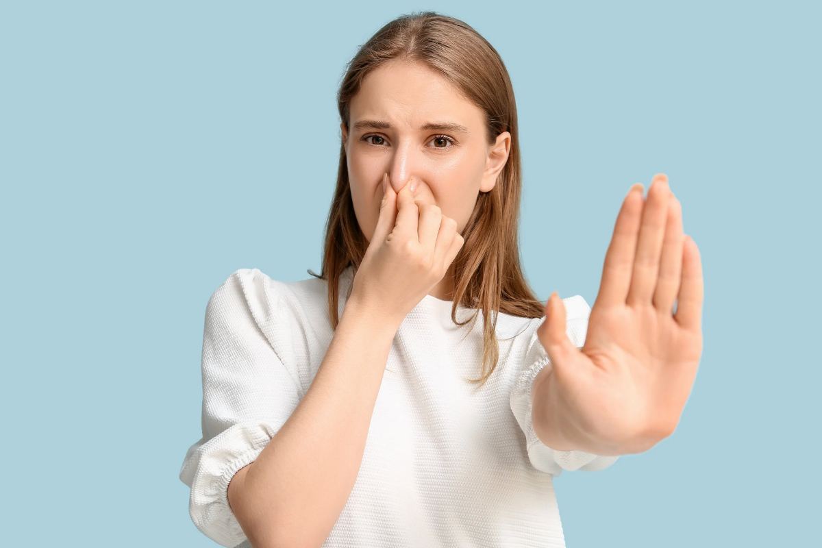 Donna che chiude il naso con le dita e mette una mano in avanti