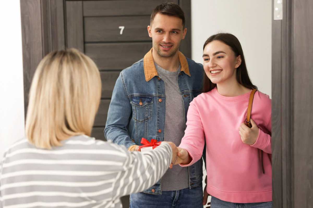 Una donna che dà un regalo a una giovaner coppia sulla porta di casa