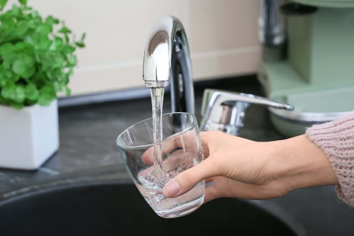 Persona che riempie un bicchiere con acqua del rubinetto