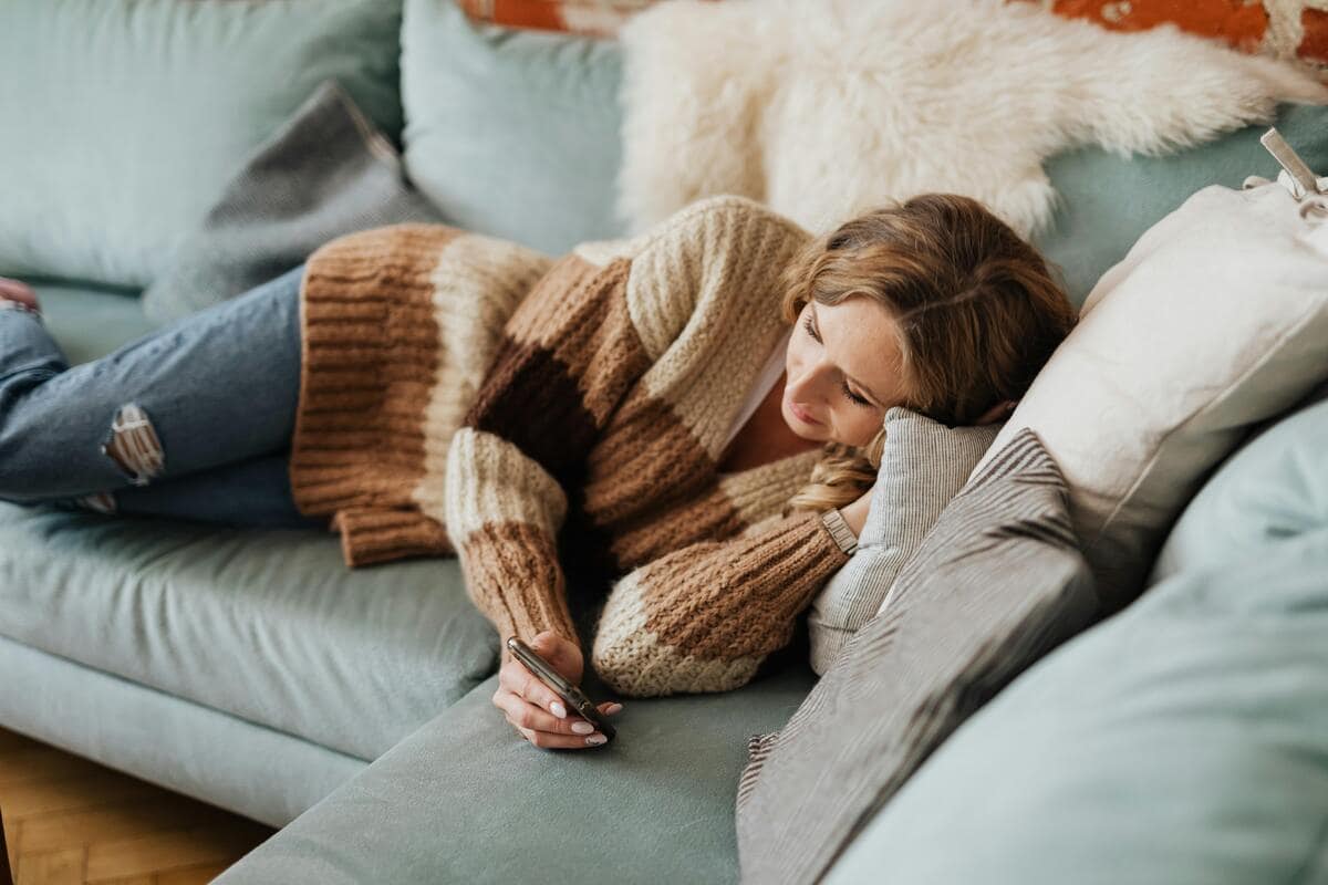 Donna stesa sul divano che guarda lo smartphone